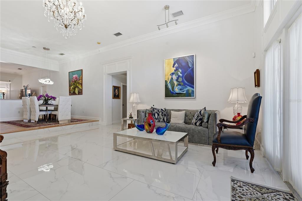 A bright living room features white marble floors, a grey sofa, and a crystal chandelier — 121 HARBOR VIEW LANE, BELLEAIR BLUFFS, FL