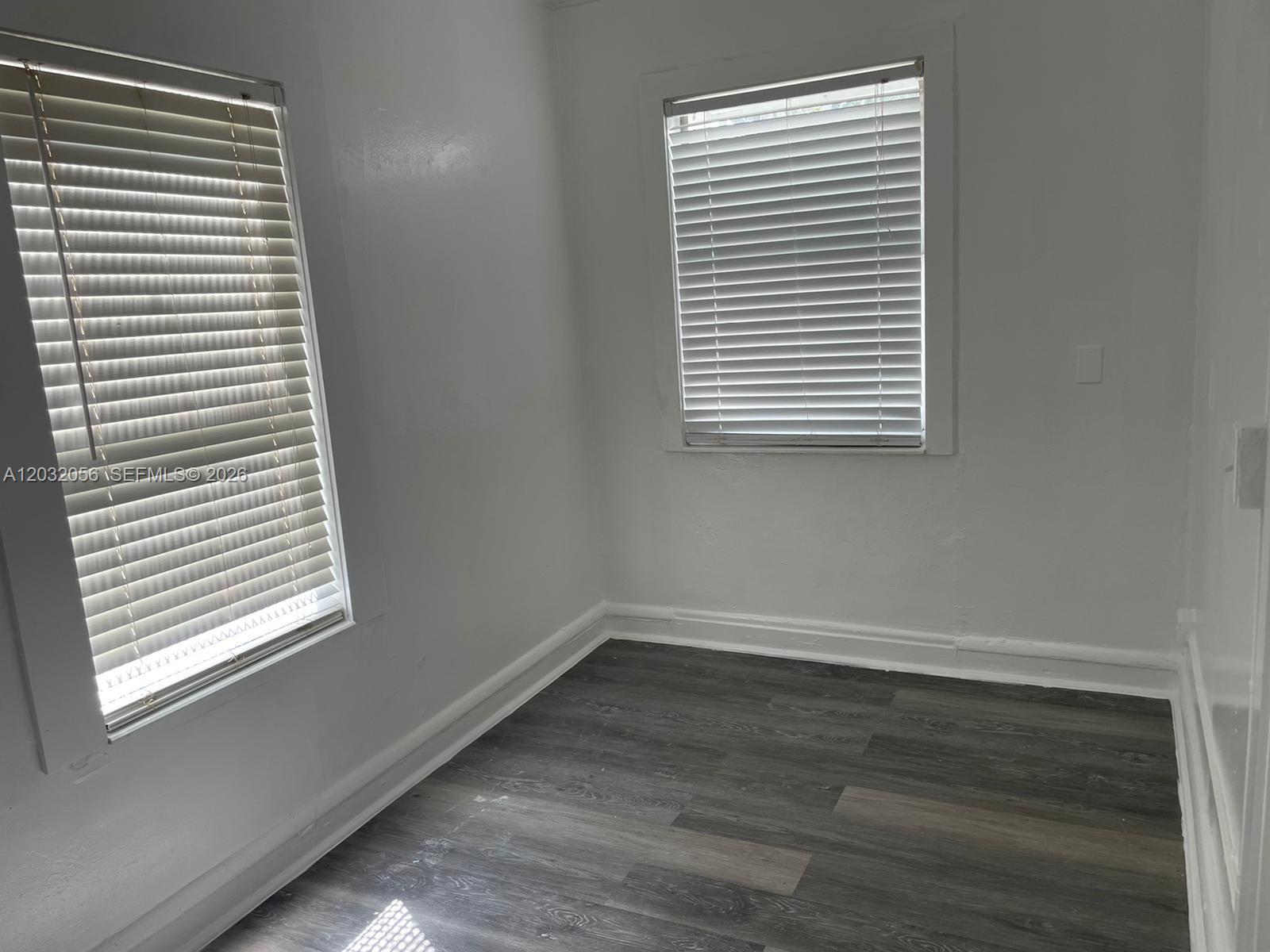 An empty room features white walls, two windows with blinds, and dark wood-look flooring — 817 4th St # 817, West Palm Beach FL 33401, WEST PALM BEACH, FL