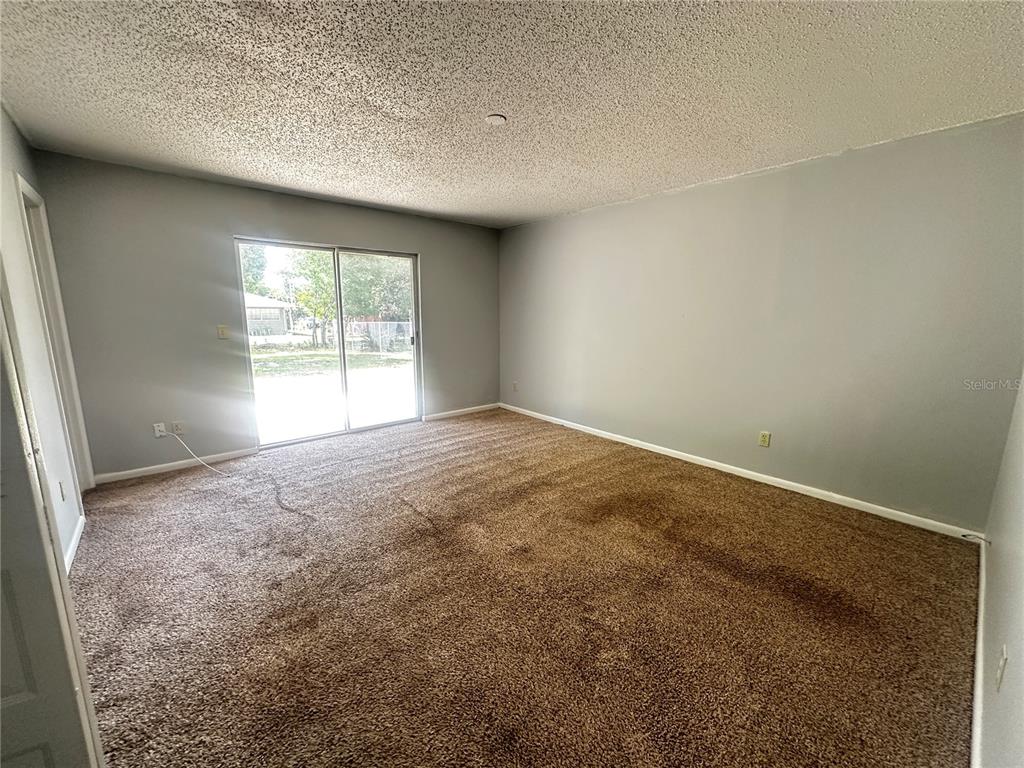 An empty room features gray walls, brown carpeting, and a sliding glass door — 455 WATER ROAD, OCALA, FL