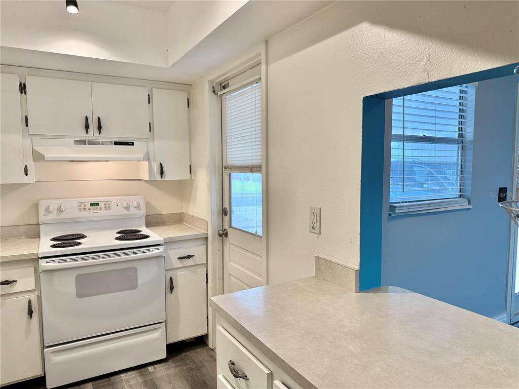 A kitchen features white cabinets, a white stove, and a countertop with a pass-through window — 2217 HOPKINS DRIVE W, BRADENTON, FL