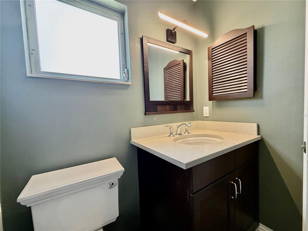 A bathroom features a dark wood vanity with a light countertop, mirror, and louvered cabinet — 2217 HOPKINS DRIVE W, BRADENTON, FL