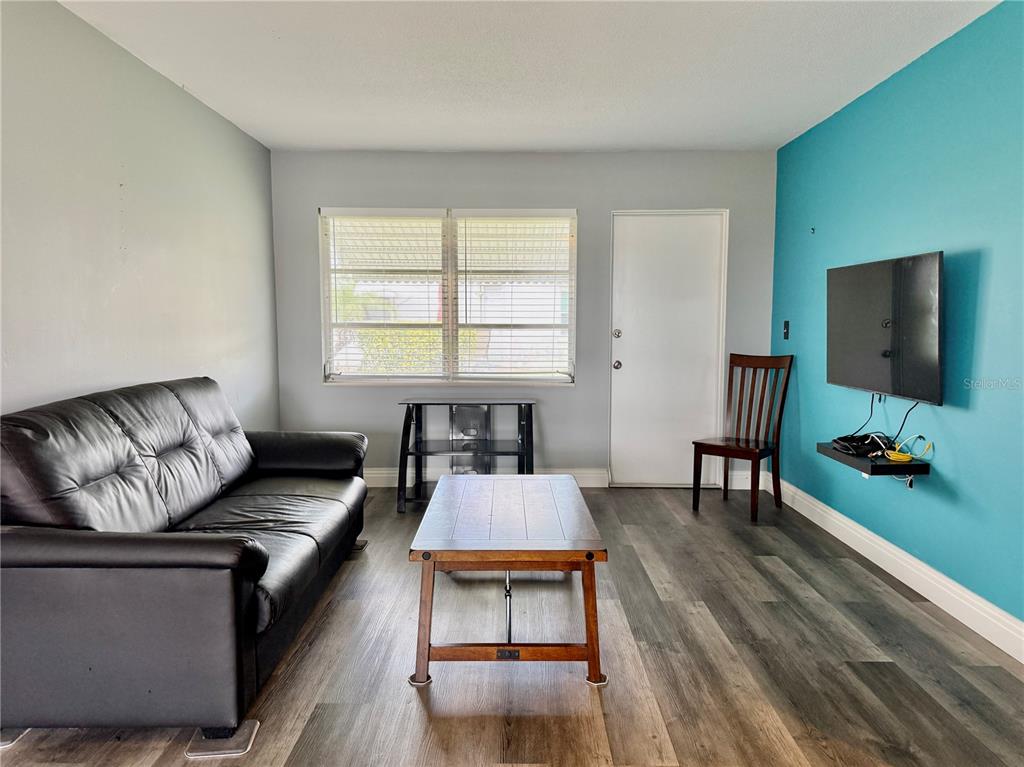 A living room features a black leather sofa, wood coffee table, and a teal accent wall — 2217 HOPKINS DRIVE W, BRADENTON, FL