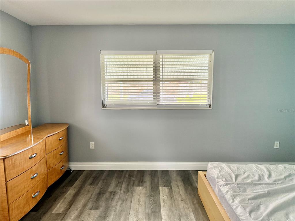 A bedroom features gray walls, wood-look flooring, a wooden dresser with a mirror, and a window — 2217 HOPKINS DRIVE W, BRADENTON, FL