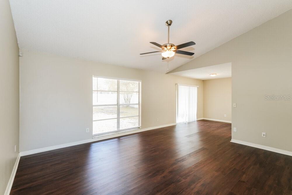 An empty living room features dark wood-look flooring, a ceiling fan, and a large window — 1670 PALM LEAF DRIVE, BRANDON, FL