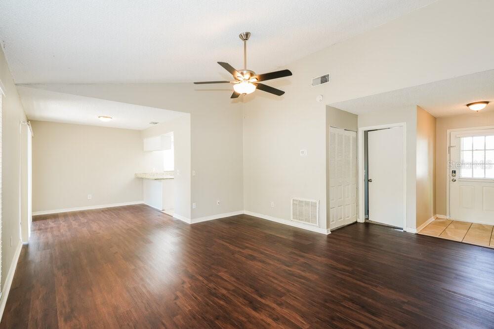 An open living area features dark wood-look flooring, a ceiling fan, and a kitchen pass-through — 1670 PALM LEAF DRIVE, BRANDON, FL