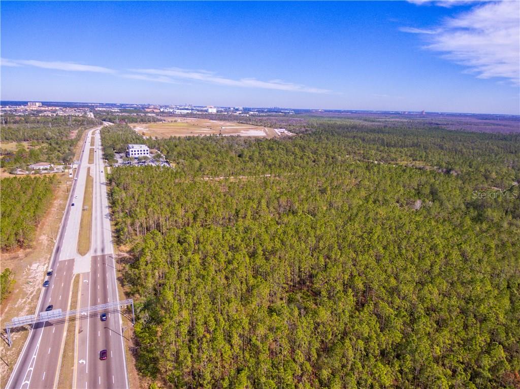 An aerial view shows a multi-lane highway running alongside a large, undeveloped wooded area — INTERNATIONAL DRIVE, ORLANDO, FL