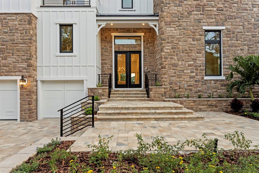 The exterior of a modern home features stone siding, white vertical panels, and a paved entryway — 4624 W SAN JOSE STREET, TAMPA, FL