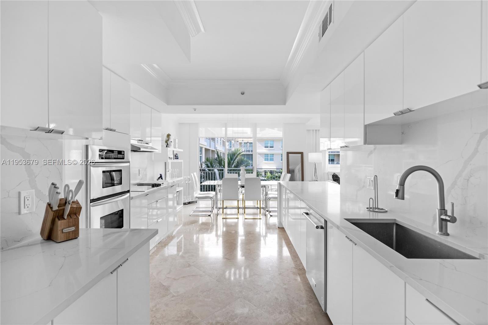 A modern, all-white kitchen features glossy cabinetry, marble countertops, and a view of the outdoors — 99 SE Mizner Blvd, Boca Raton FL 33432, BOCA RATON, FL