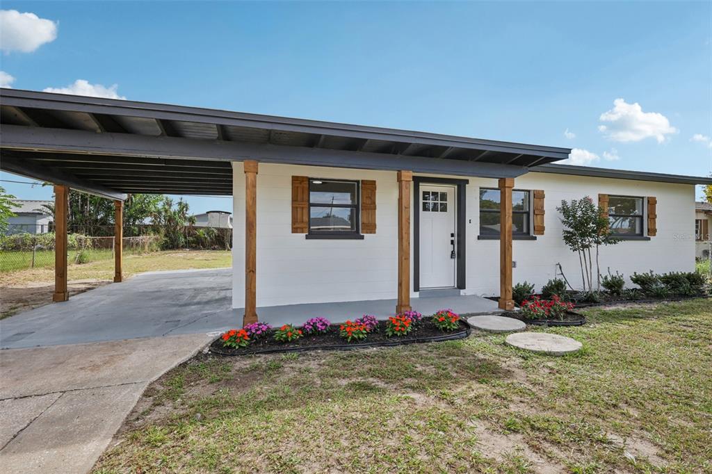 A single-story white house features a carport, wooden support posts, and a front flower bed — 2633 ROYAL DRIVE, LAKELAND, FL