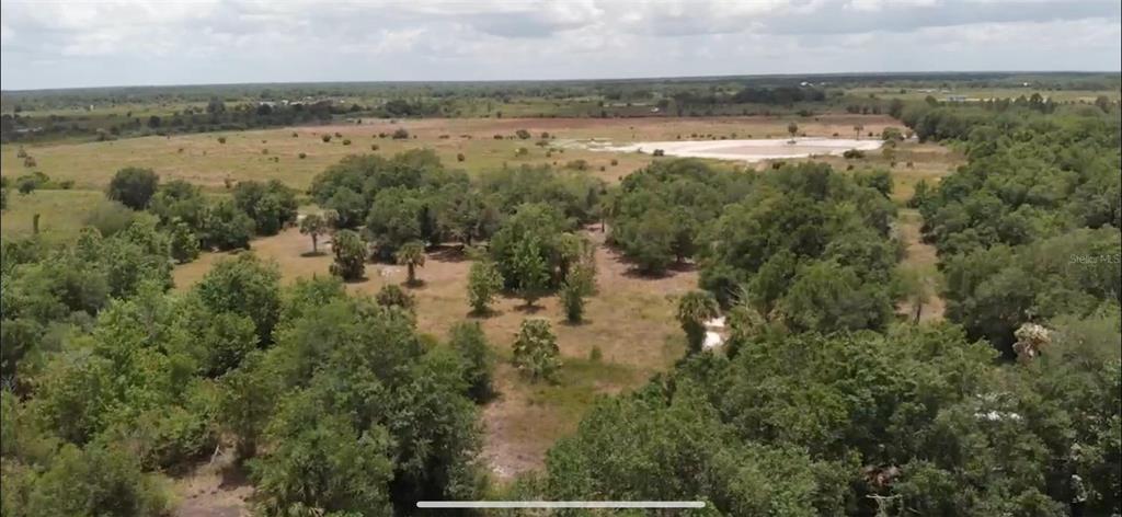 An aerial view shows a large, grassy lot with scattered trees and a distant pond — 21914 NW 286TH STREET, OKEECHOBEE, FL