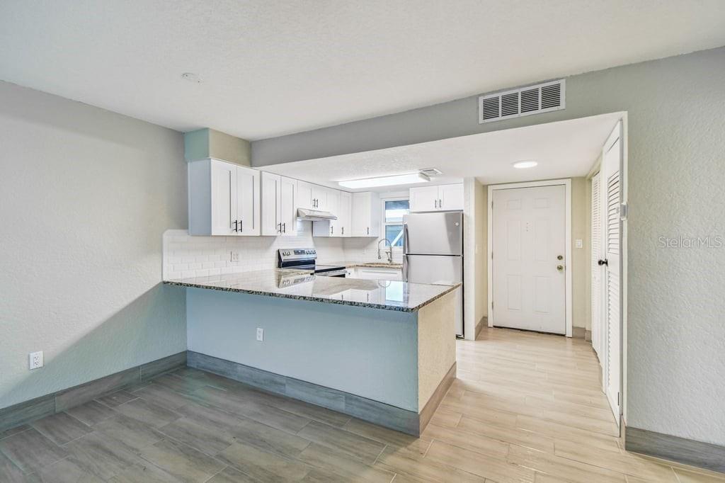 A kitchen features white cabinets, granite countertops, a breakfast bar, and light-colored tile flooring — 4829 ONYX LANE UNIT 101, NEW PORT RICHEY, FL