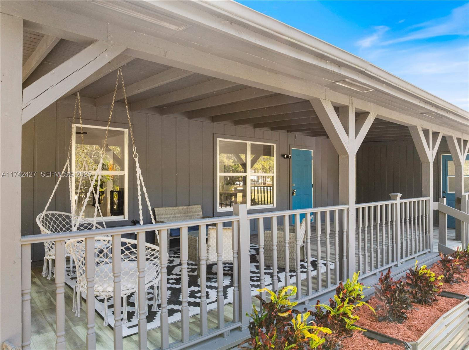 A gray house features a covered porch with a white railing and hanging chairs — 11448 N 68th St Street N, FL 33412, FL