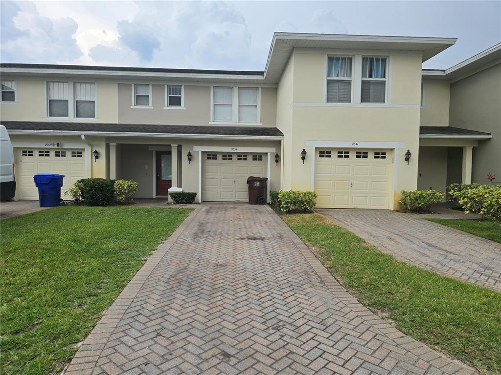 A row of three attached townhouses with paved driveways, garages, and light-colored stucco exteriors — 2039 CYPRESS BAY BOULEVARD, KISSIMMEE, FL