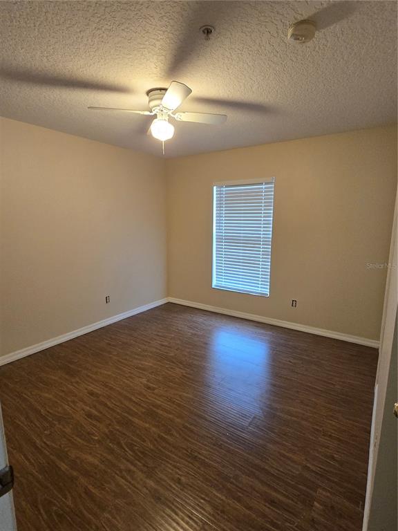 An empty bedroom with beige walls, wood-look flooring, a ceiling fan, and a window — 2039 CYPRESS BAY BOULEVARD, KISSIMMEE, FL
