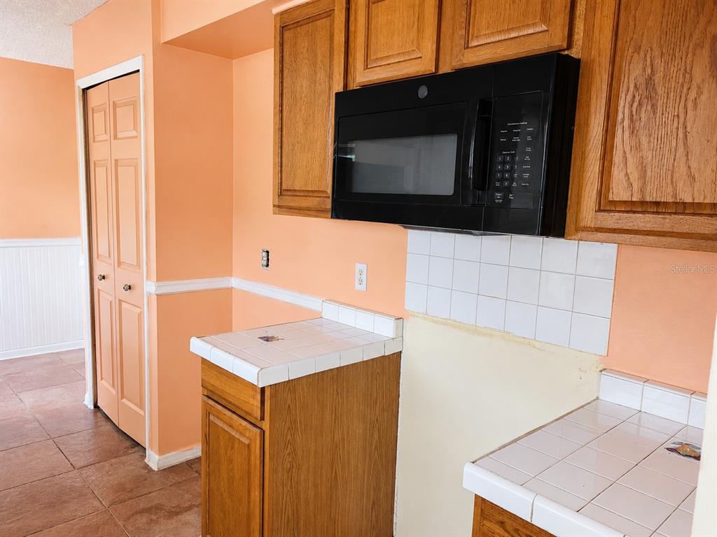 A kitchen features oak cabinets, a black microwave, tiled countertops, and peach-colored walls — 765 HIGHLAND DRIVE, ORANGE CITY, FL