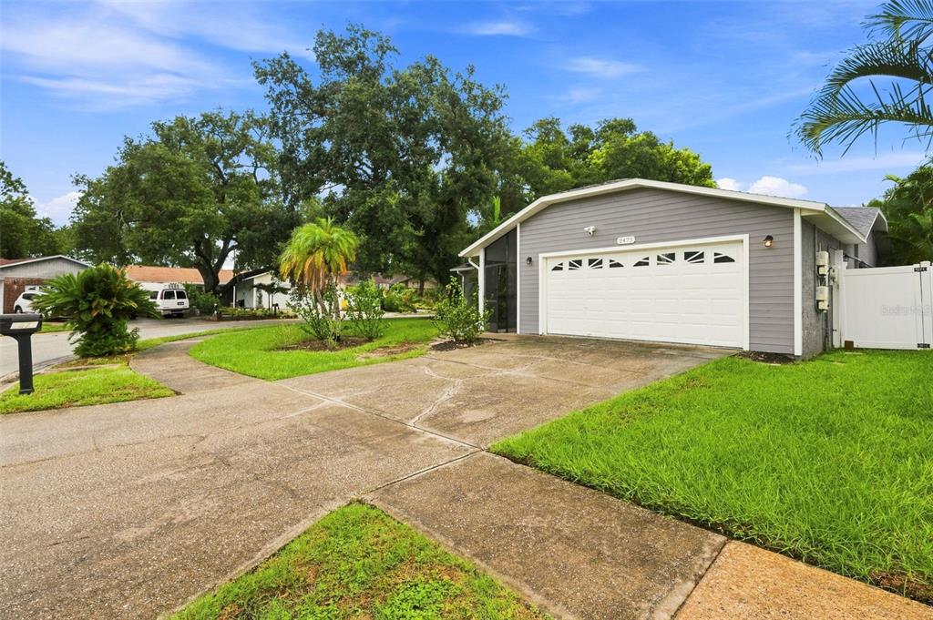 A gray house exterior features a white garage door, a concrete driveway, and green landscaping — 2475 GULFBREEZE CIRCLE, PALM HARBOR, FL