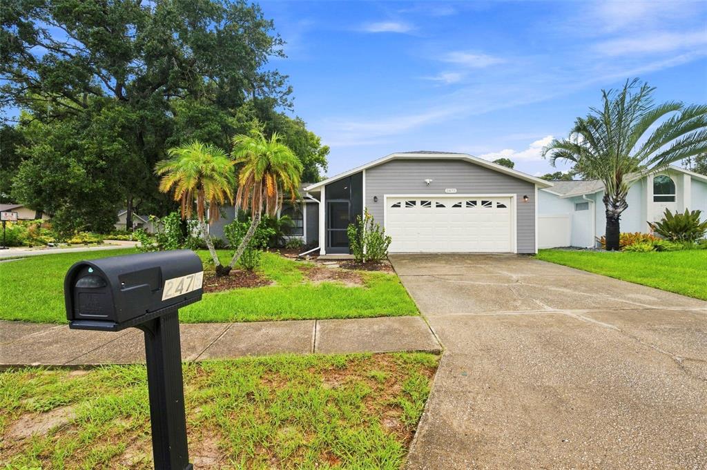 A single-story house with gray siding, a two-car garage, and a front lawn with palms — 2475 GULFBREEZE CIRCLE, PALM HARBOR, FL