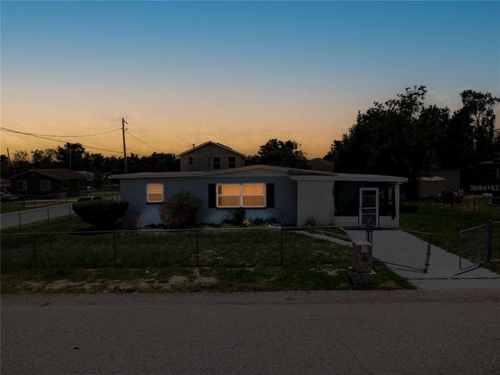 A single-story house with a fenced yard is shown at dusk under a sunset sky — 1125 AVENUE L, HAINES CITY, FL