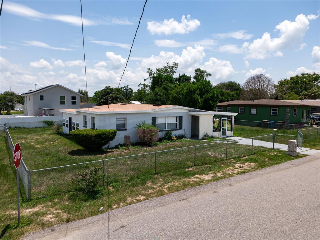 A single-story white brick house with a flat roof sits behind a chain-link fence — 1125 AVENUE L, HAINES CITY, FL