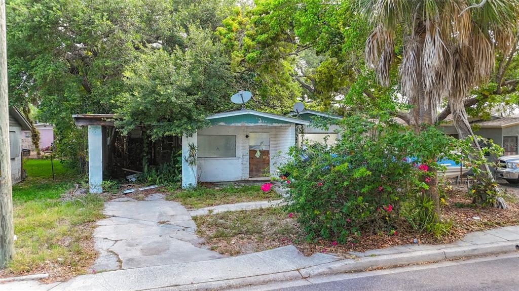 A weathered, single-story house with a covered porch and overgrown landscaping sits near a street — 1679 24TH STREET, SARASOTA, FL