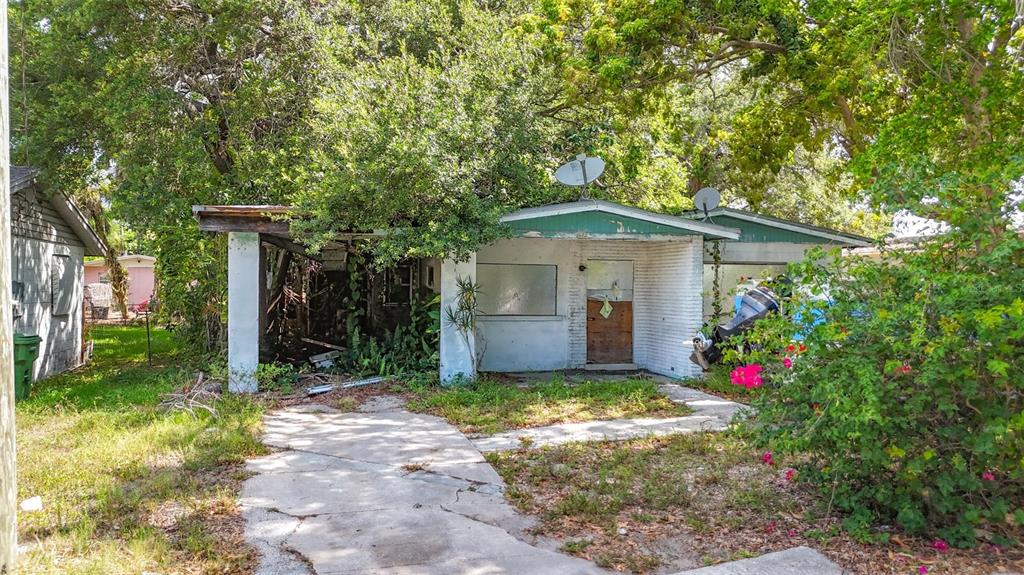A weathered, single-story house with a carport, boarded-up windows, and overgrown landscaping — 1679 24TH STREET, SARASOTA, FL