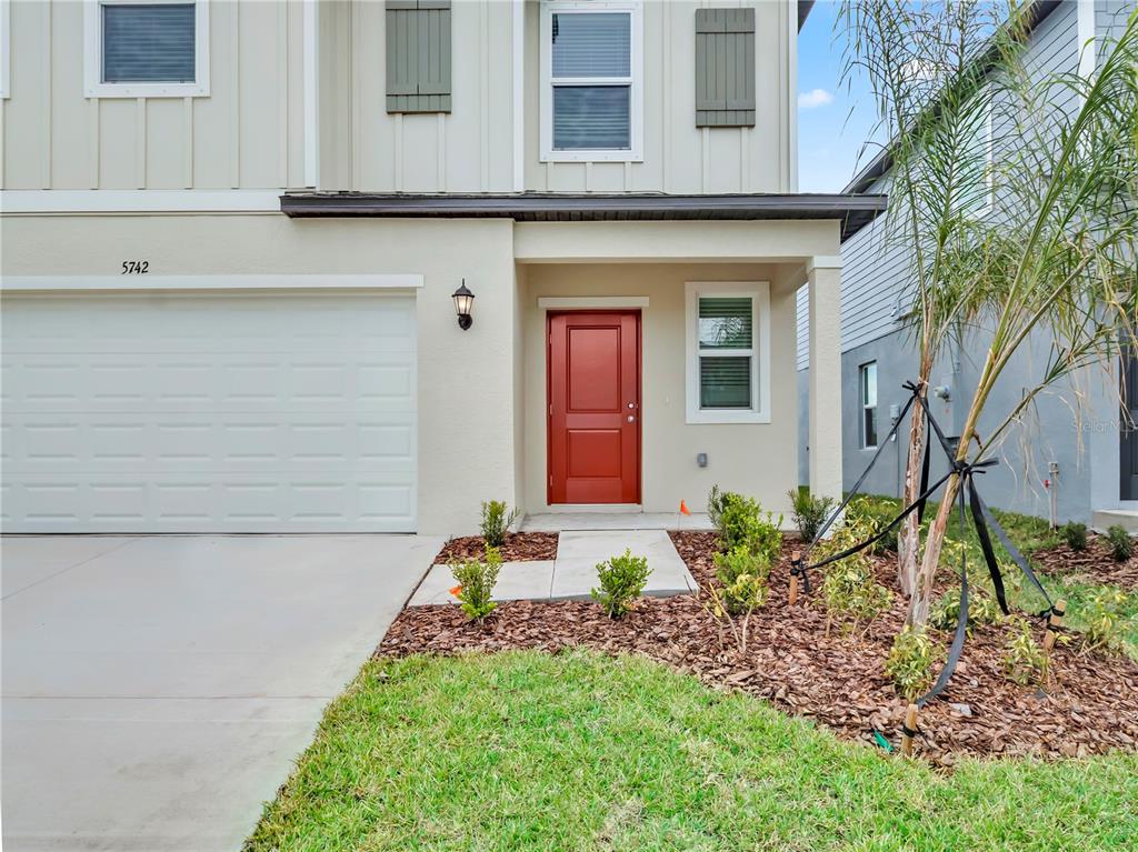 A two-story house exterior features a white garage door, a red front door, and landscaping — 5771 RED KITE DRIVE, WIMAUMA, FL