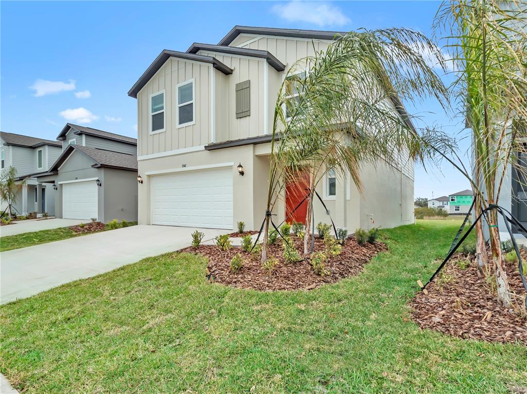 A two-story suburban house with a beige exterior, a two-car garage, and a red door — 5771 RED KITE DRIVE, WIMAUMA, FL