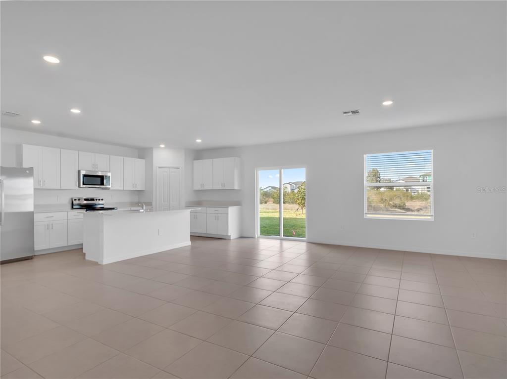An open-concept kitchen and living area features white cabinetry, tile flooring, and sliding glass doors — 5771 RED KITE DRIVE, WIMAUMA, FL