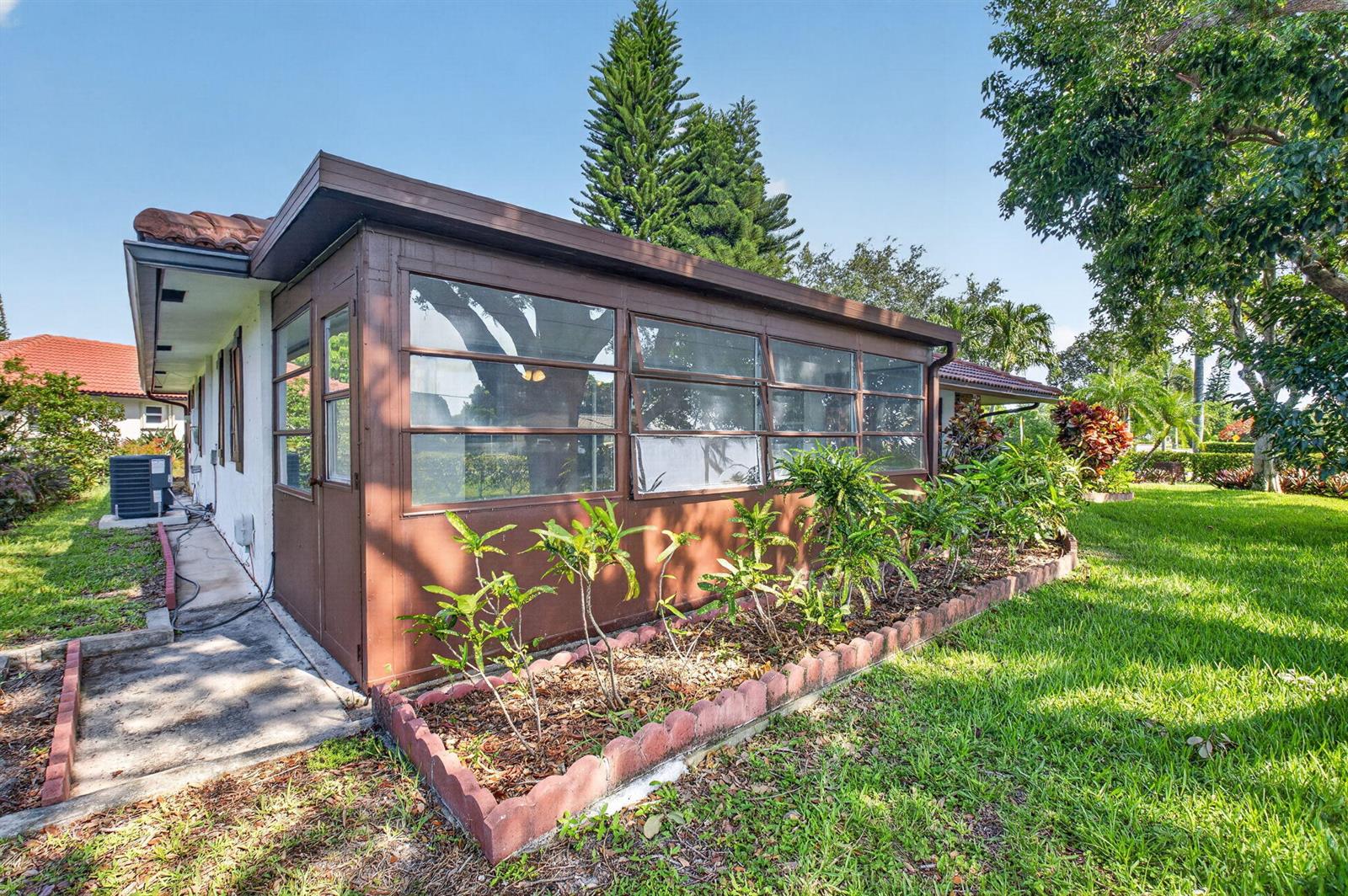 A brown sunroom with large windows sits on the side of a house with landscaping — 300 NW 42nd Street, Boca Raton FL 33431, BOCA RATON, FL