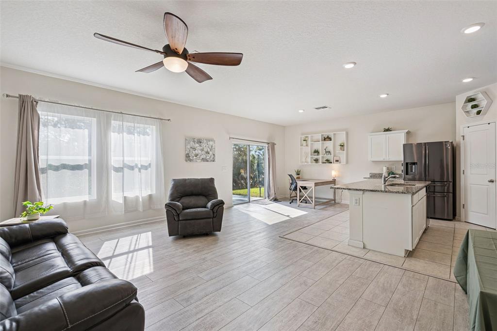 An open-concept living room and kitchen featuring light wood-look flooring and a ceiling fan — 2044 CADES COVE WAY, DELAND, FL