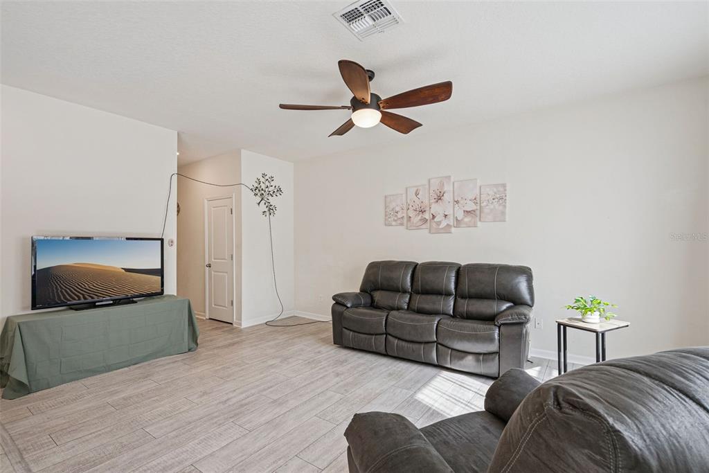 A living room features gray tile flooring, a dark leather sofa, and a ceiling fan — 2044 CADES COVE WAY, DELAND, FL