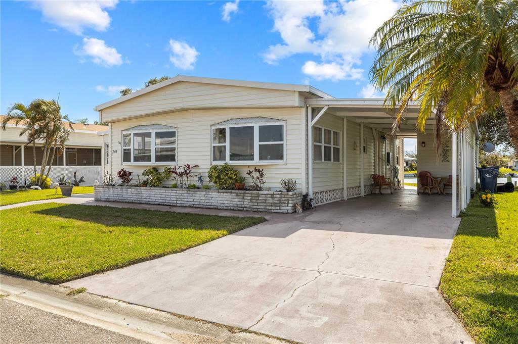 A single-story manufactured home features light siding, a concrete driveway, and a covered carport — 204 51ST AVENUE E, BRADENTON, FL