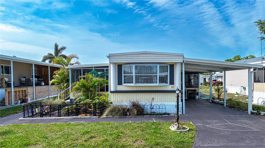 A single-story manufactured home features a front porch, a carport, and a small landscaped yard — 420 49TH STREET E UNIT 83, PALMETTO, FL