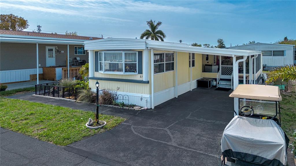 A yellow mobile home with a carport and a golf cart parked in the driveway — 420 49TH STREET E UNIT 83, PALMETTO, FL