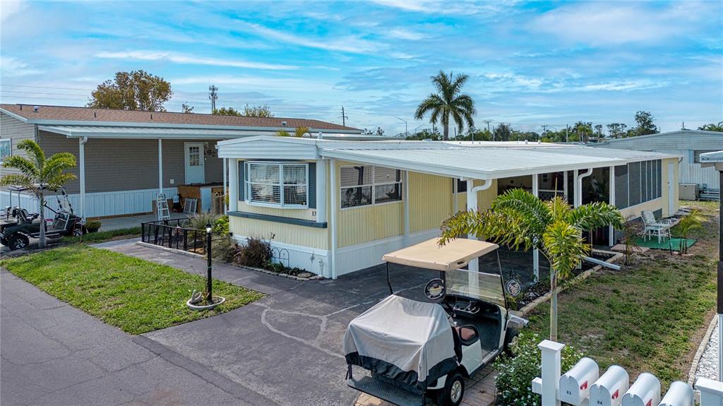A yellow mobile home features a covered carport, a golf cart, and a palm tree — 420 49TH STREET E UNIT 83, PALMETTO, FL