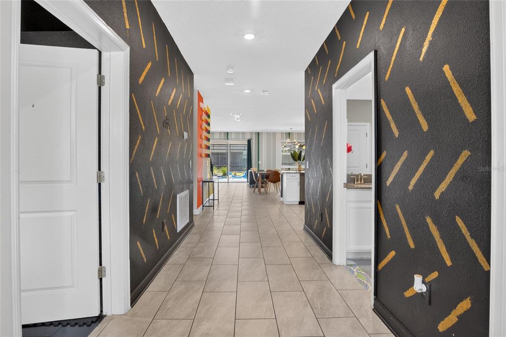 A hallway with black walls featuring gold brushstroke patterns leads toward an open-concept living area — 4536 TARGET BOULEVARD, KISSIMMEE, FL