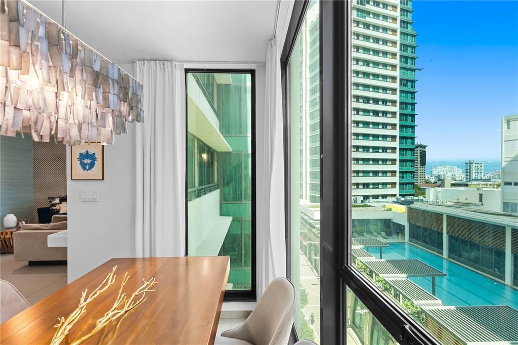 A dining area with a modern chandelier overlooks a high-rise building and an outdoor pool — 1511 PONCE DE LEON AVENUE UNIT 851, SAN JUAN, PR