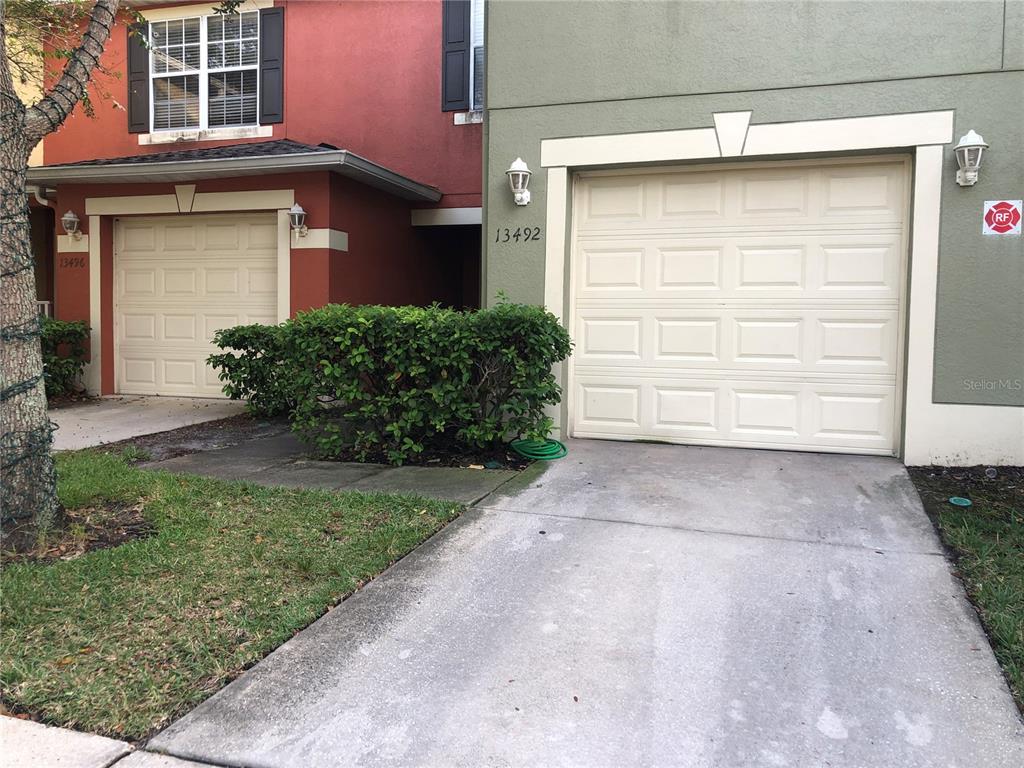 The exterior of two adjacent townhomes features beige garage doors, concrete driveways, and green landscaping — 13492 APPLEROSE LANE UNIT 22, ORLANDO, FL