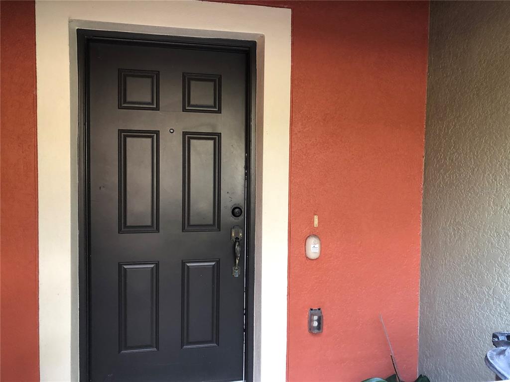 A dark-colored front door with a peephole is set into a textured orange exterior wall — 13492 APPLEROSE LANE UNIT 22, ORLANDO, FL