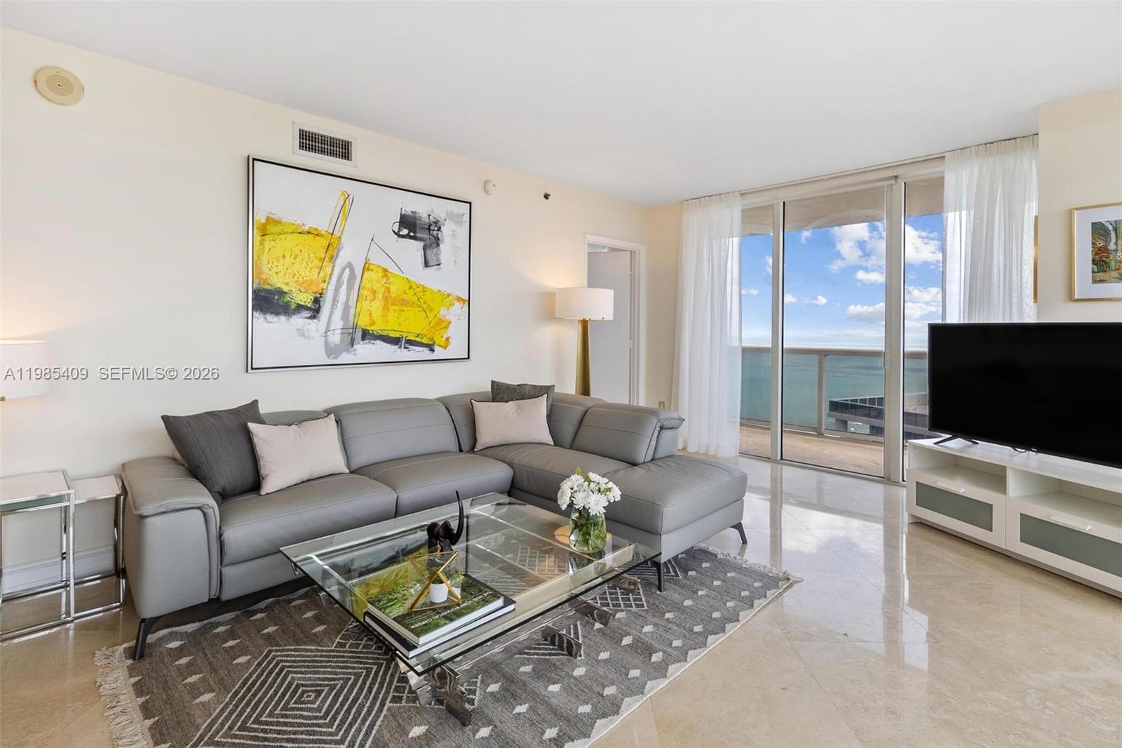 A living room features a gray sectional sofa, glass coffee table, and ocean view balcony — 1830 S Ocean Dr # 4706, Hallandale Beach FL 33009, HALLANDALE BEACH, FL