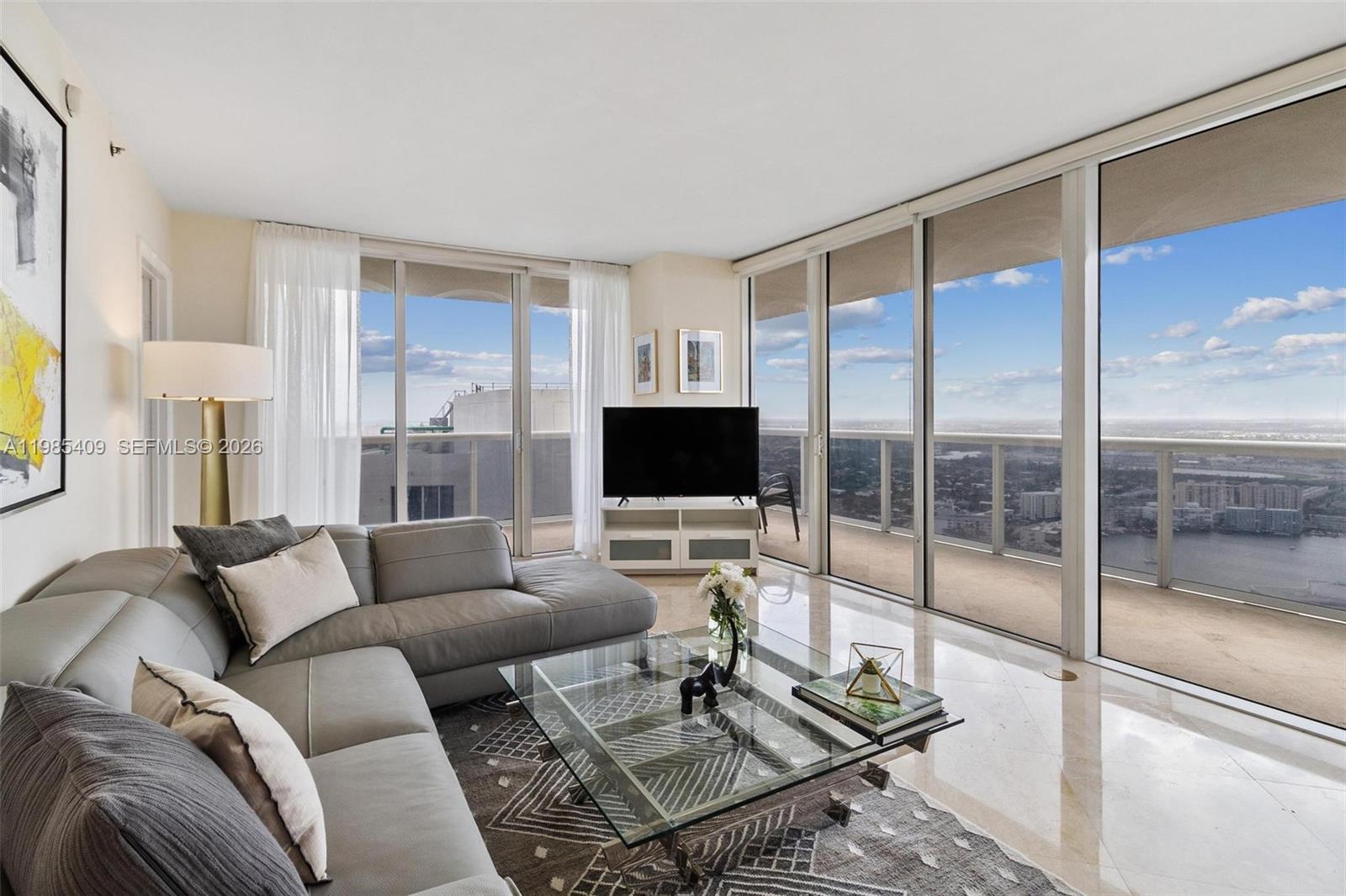 A living room features a grey sectional sofa, glass coffee table, and floor-to-ceiling windows — 1830 S Ocean Dr # 4706, Hallandale Beach FL 33009, HALLANDALE BEACH, FL