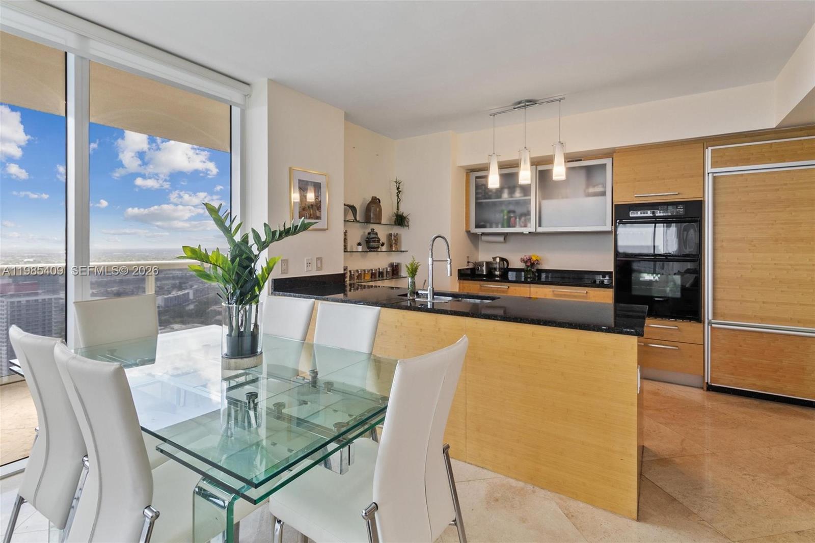 A modern kitchen features light wood cabinetry, black granite countertops, and a glass dining table — 1830 S Ocean Dr # 4706, Hallandale Beach FL 33009, HALLANDALE BEACH, FL