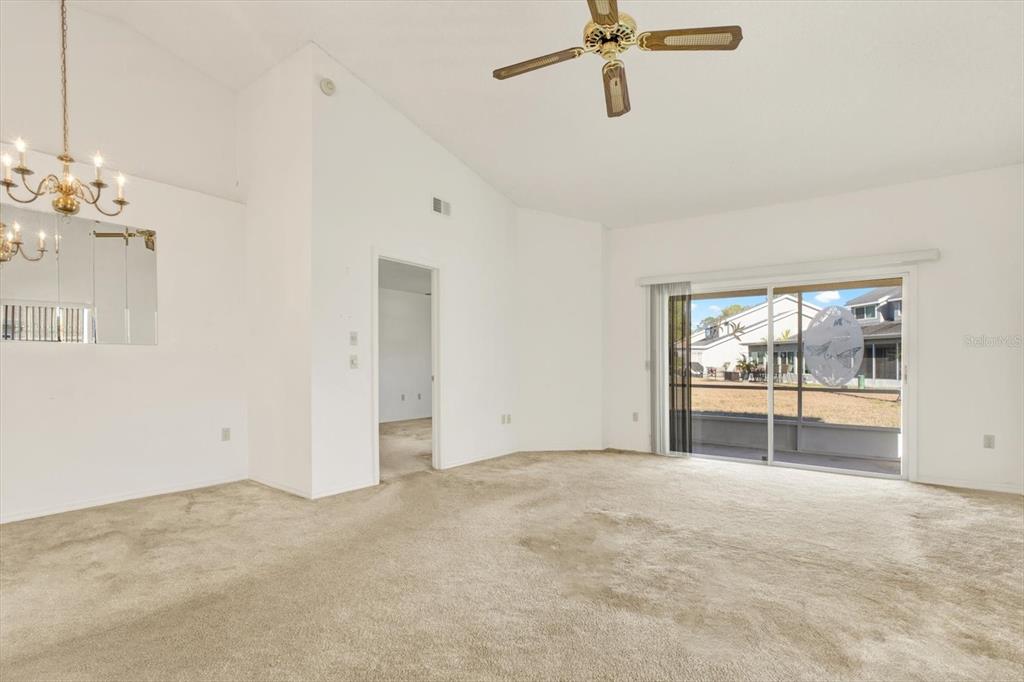 A living room with beige carpet, a ceiling fan, and sliding glass doors to a patio — 4208 BOSTON CIRCLE, NEW PORT RICHEY, FL