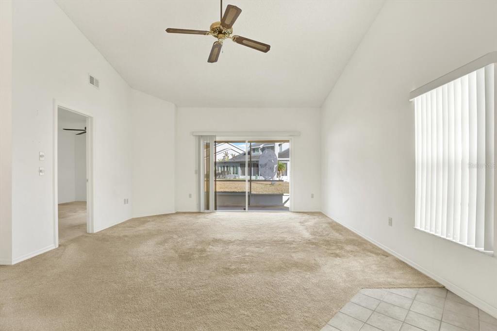 A living room with beige carpeting, a vaulted ceiling, a ceiling fan, and sliding glass doors — 4208 BOSTON CIRCLE, NEW PORT RICHEY, FL