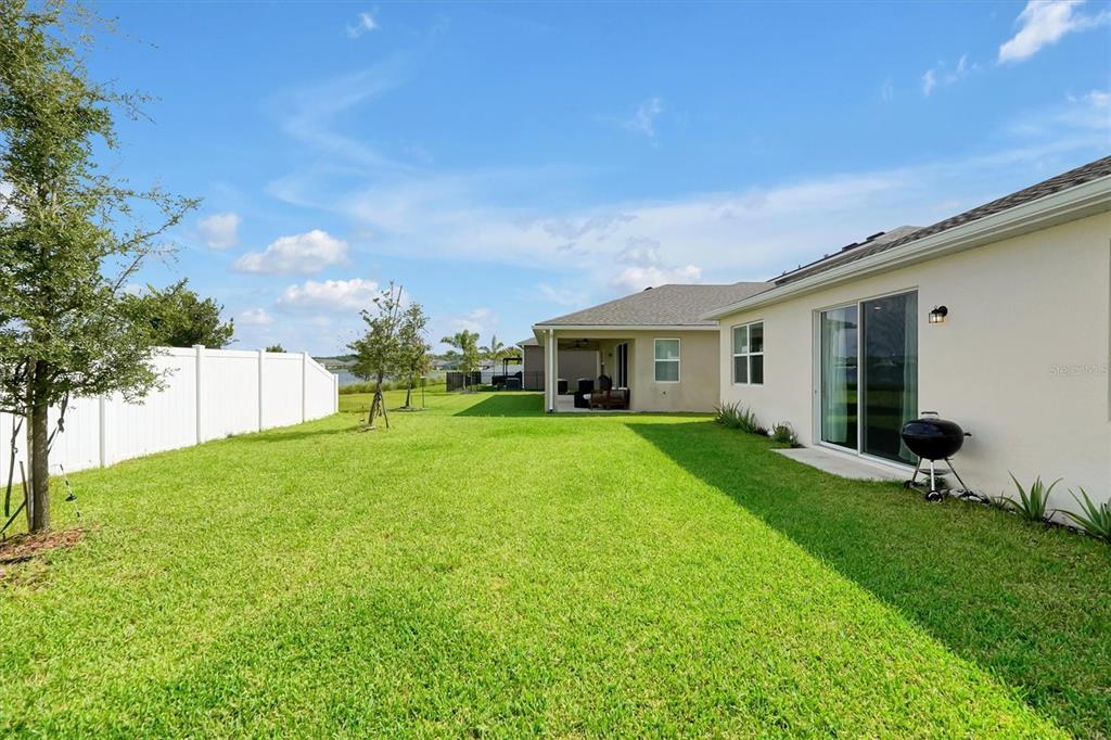 A backyard with a green lawn, white vinyl fence, and a view of a lake — 8560 COMPASS POINT AVENUE, ORLANDO, FL