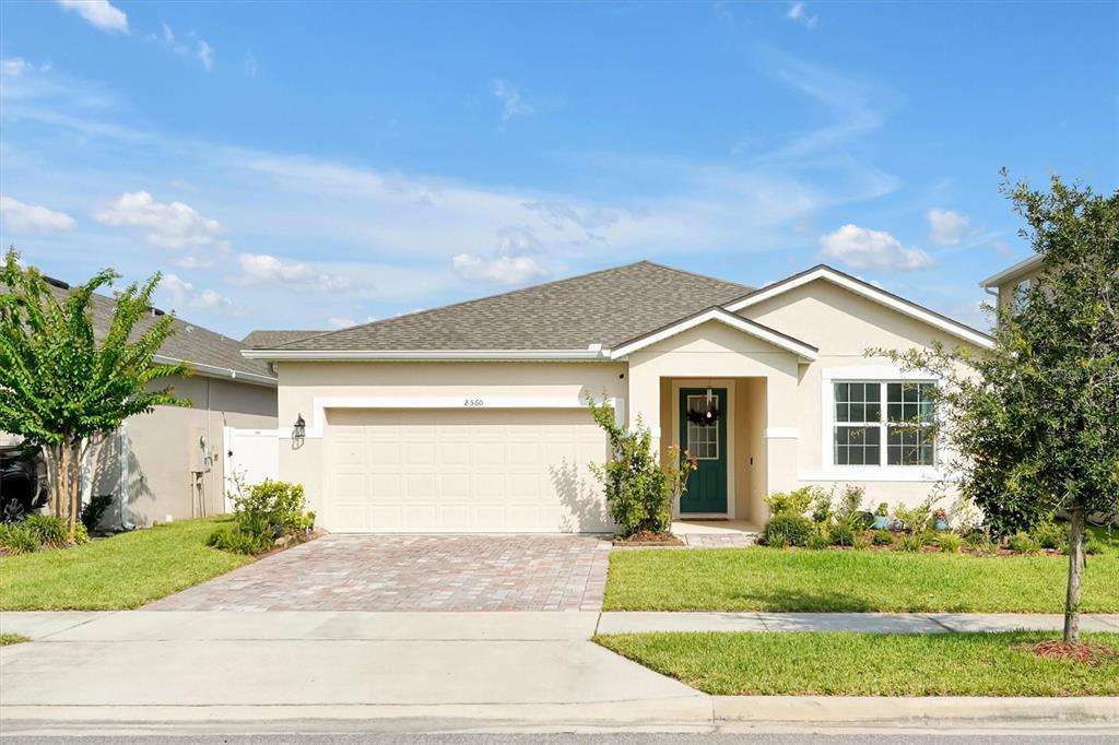 A single-story house with a beige stucco exterior, a two-car garage, and a green door — 8560 COMPASS POINT AVENUE, ORLANDO, FL