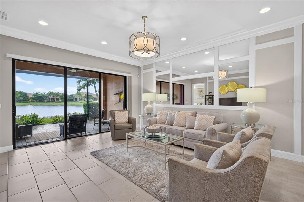A living room features tile floors, a large mirror wall, and sliding doors overlooking a lake — 11957 FIVE WATERS CIRCLE, FORT MYERS, FL