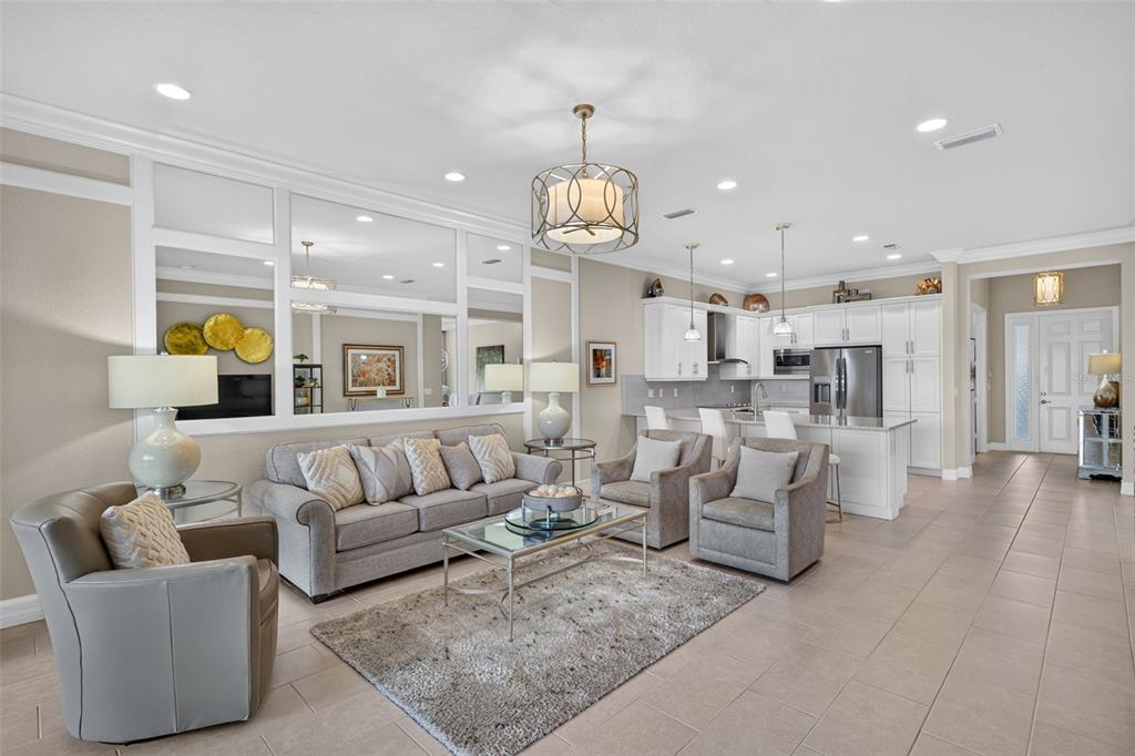 An open-concept living room and kitchen featuring neutral furniture, tiled floors, and a mirrored wall — 11957 FIVE WATERS CIRCLE, FORT MYERS, FL