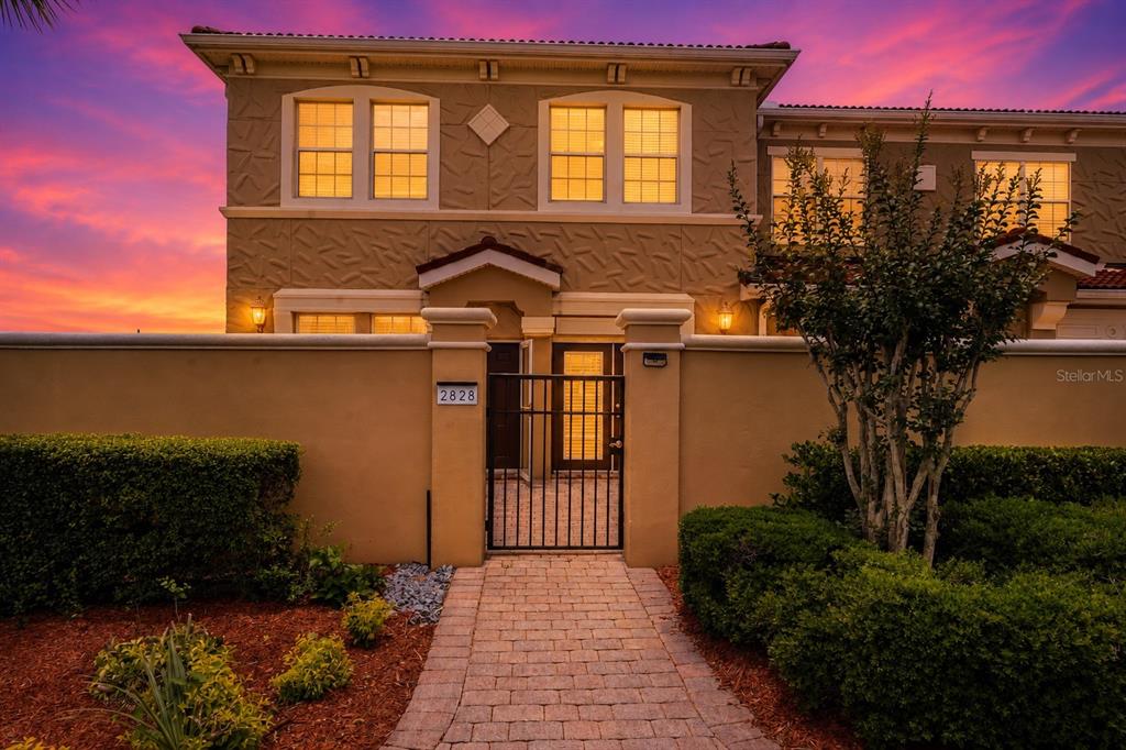 A two-story house exterior features a gated courtyard entrance and a brick walkway at sunset — 2828 BELLA VISTA DRIVE, DAVENPORT, FL