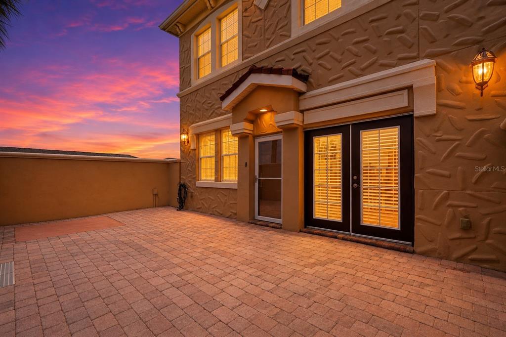 A paved patio sits beside a tan stucco house with double glass doors at sunset — 2828 BELLA VISTA DRIVE, DAVENPORT, FL